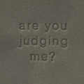 Surface Detail of original, minimalist, hand-embossed grey art card featuring the fun message ‘are you judging me?’