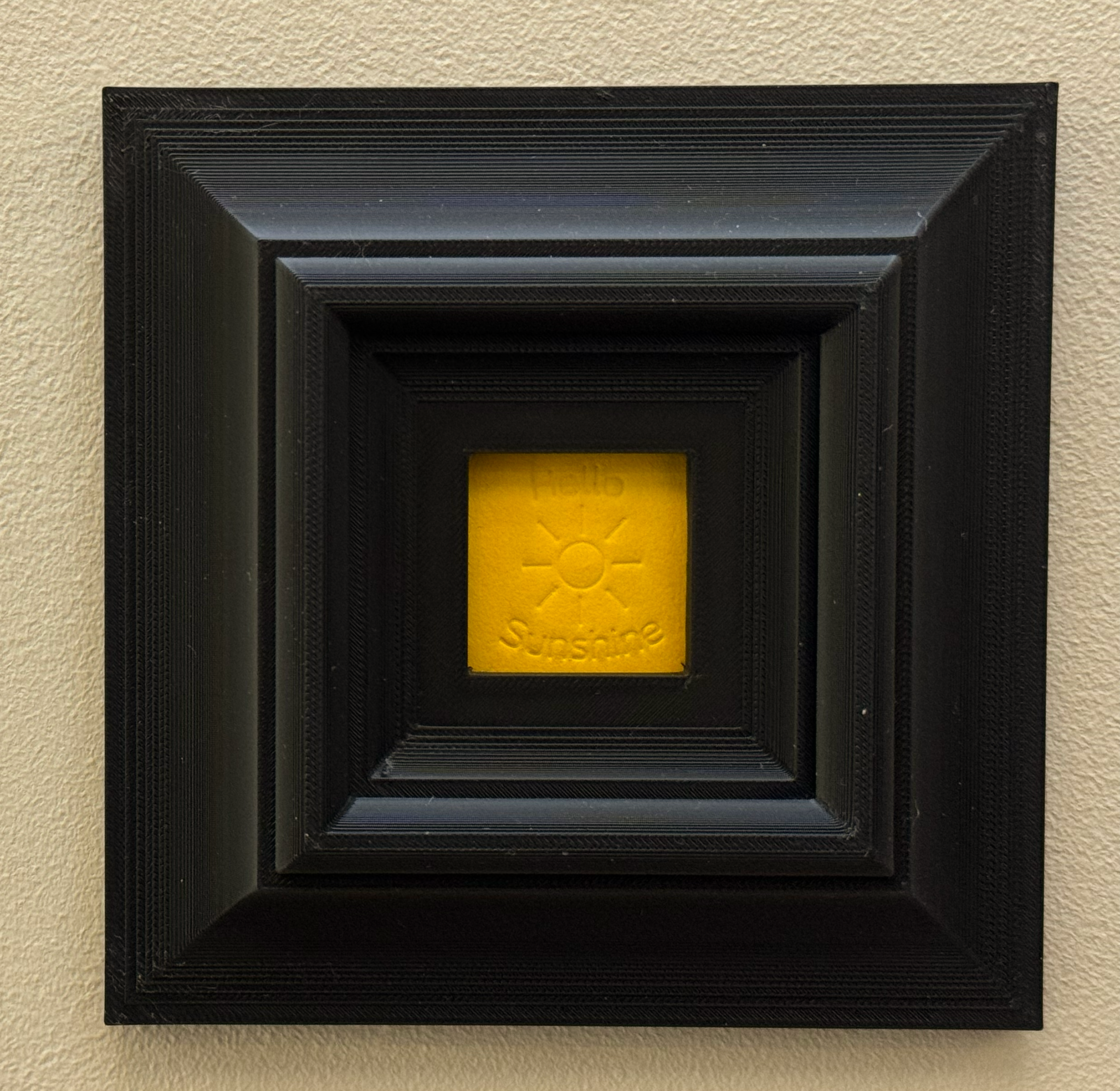 Original, minimalist, hand-embossed yellow art card featuring the positive message ‘Hello Sunshine’ demonstrating the scale of the black oversized 3d printed frame